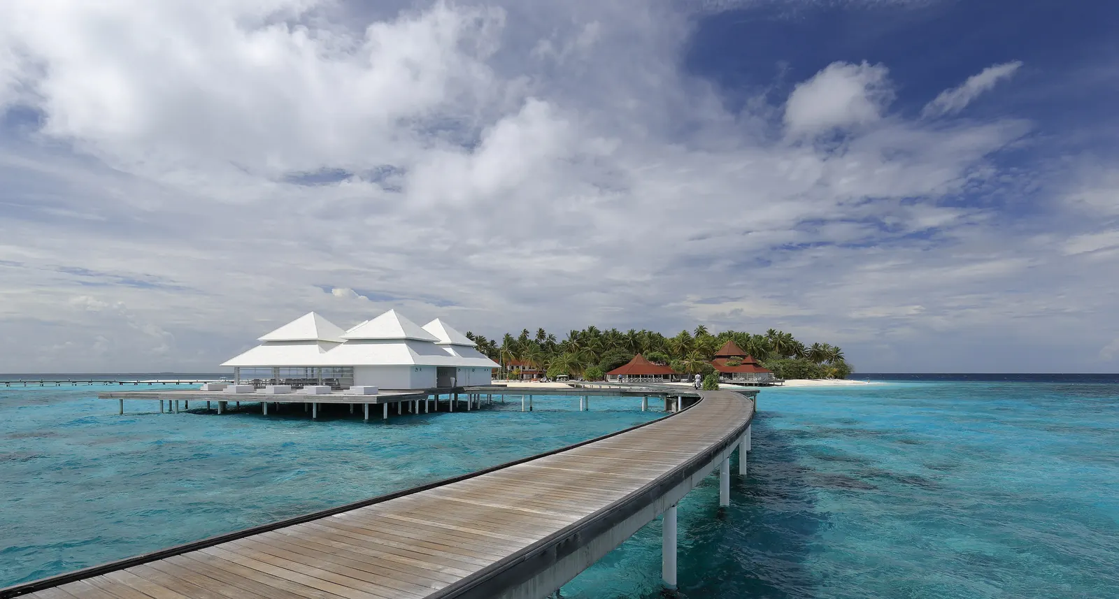 A wooden jetty leading to overwater villas above a turquoise lagoon in the Maldives